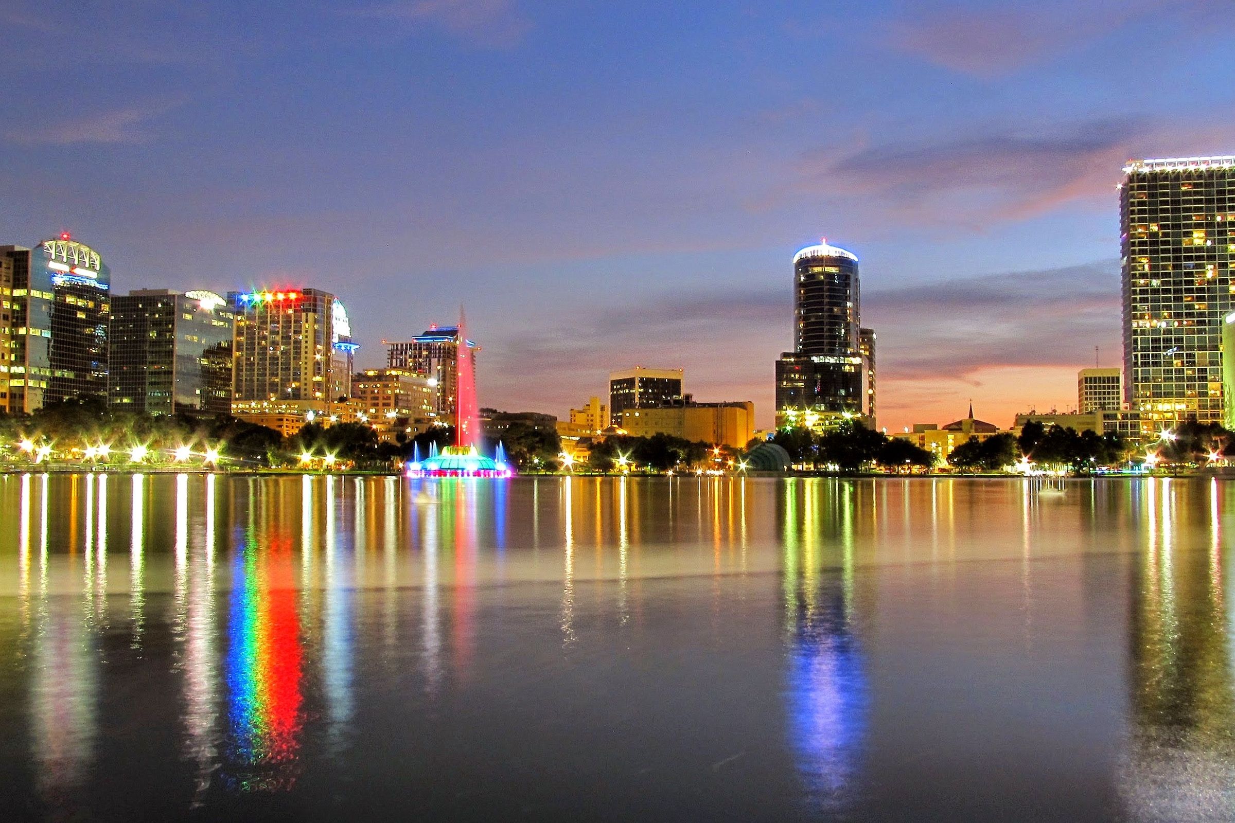 The Orlando skyline of glass office towers reflected in Lake Eola on a bright day.