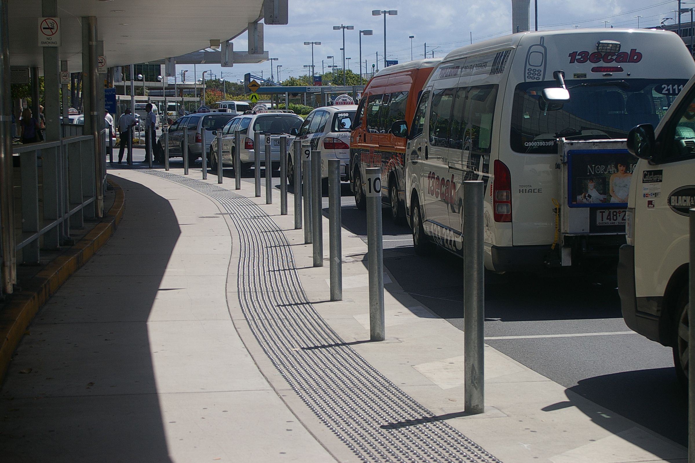 A line of shuttle vans and cars waiting along an airport ground transport kerb.