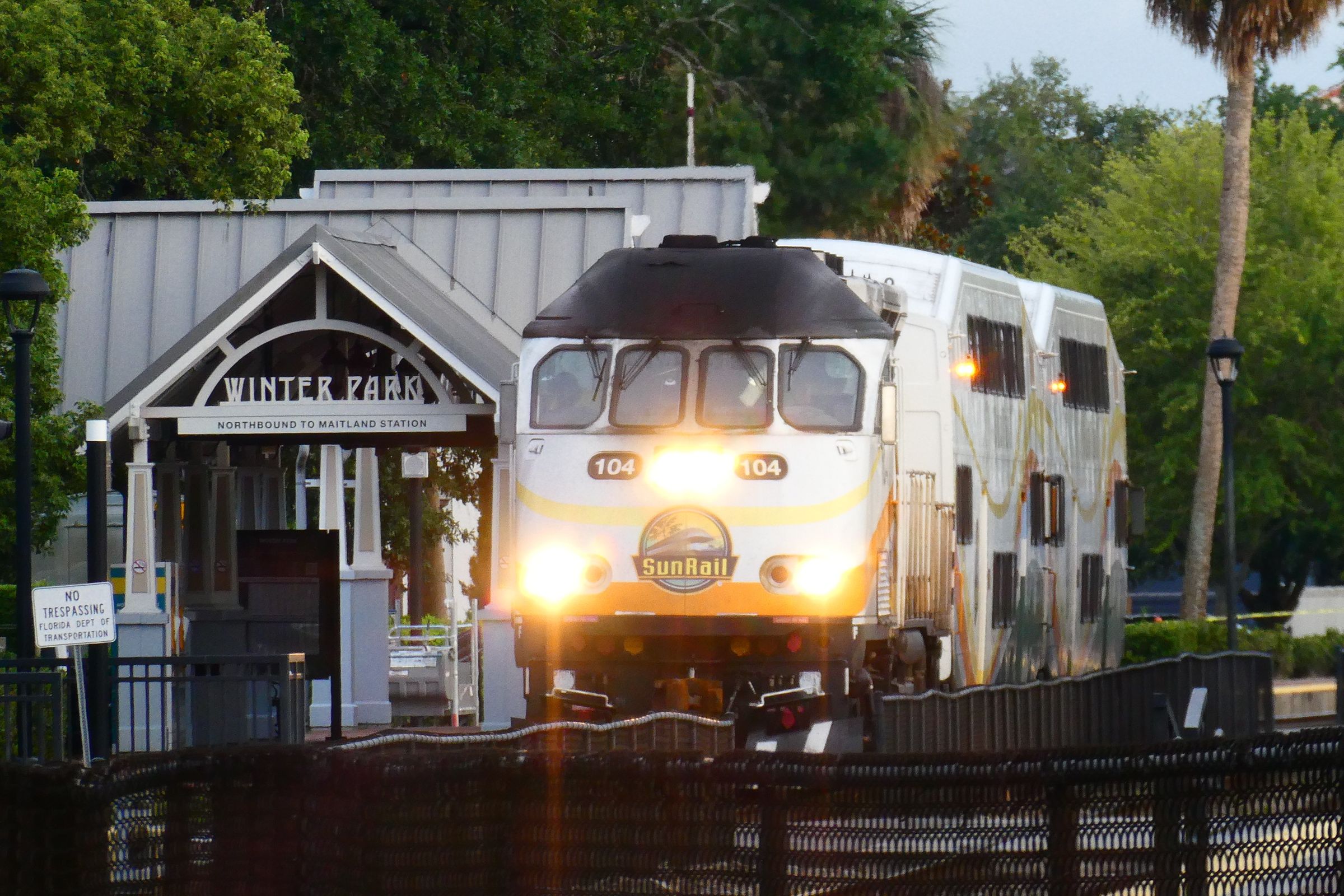A SunRail commuter train with headlights on, stopped at Winter Park station.