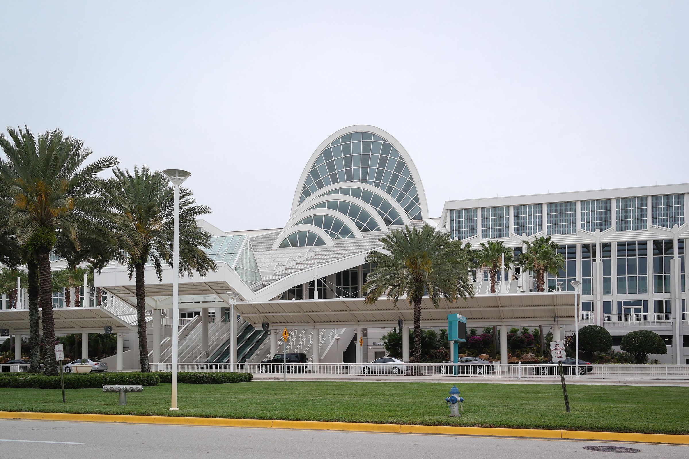 The curved glass roof of the Orange County Convention Center behind a row of palms.